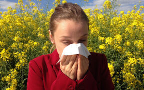 girl sneezing into a tissue in front of spring flowers