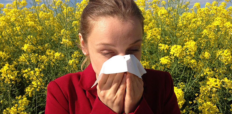 girl sneezing into a tissue in front of spring flowers