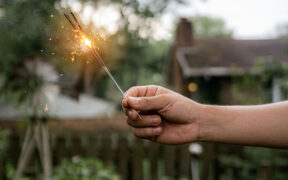 an arm holding a lit sparkler in the back yard