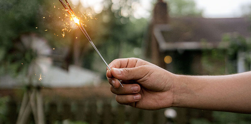 an arm holding a lit sparkler in the back yard