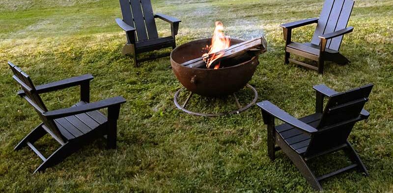 wood fire pit with 4 Adirondack chairs in a yard