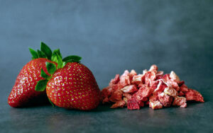 whole strawberries next to a pile of dehydrated strawberry pieces