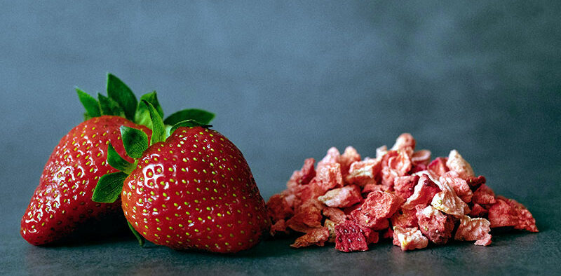 whole strawberries next to a pile of dehydrated strawberry pieces